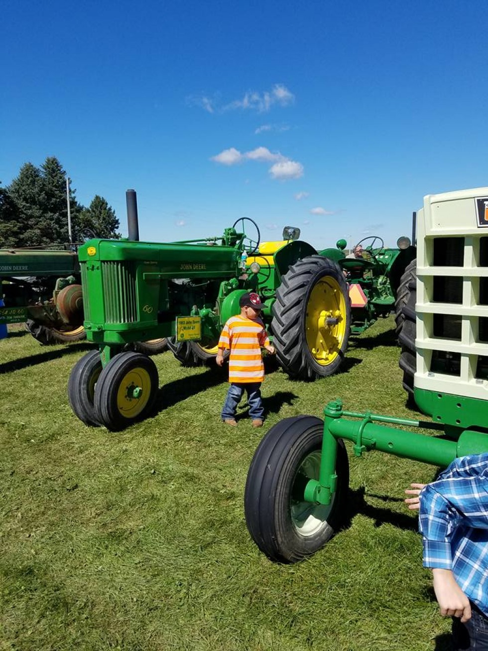 A child stands near a John Deere tractor displayed on site