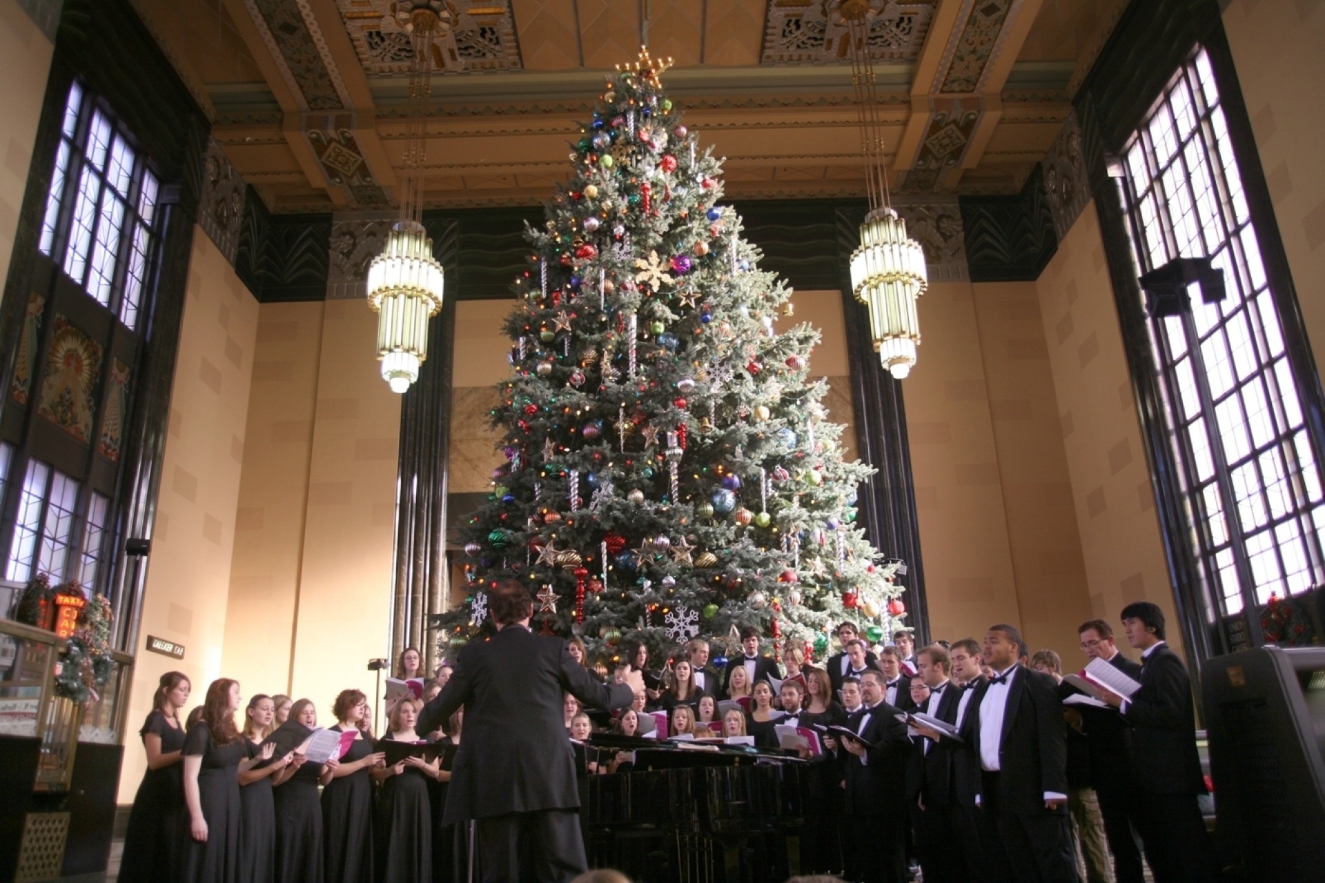 A photo of a choir singing in front of the massive christmas tree at the Durham Museum